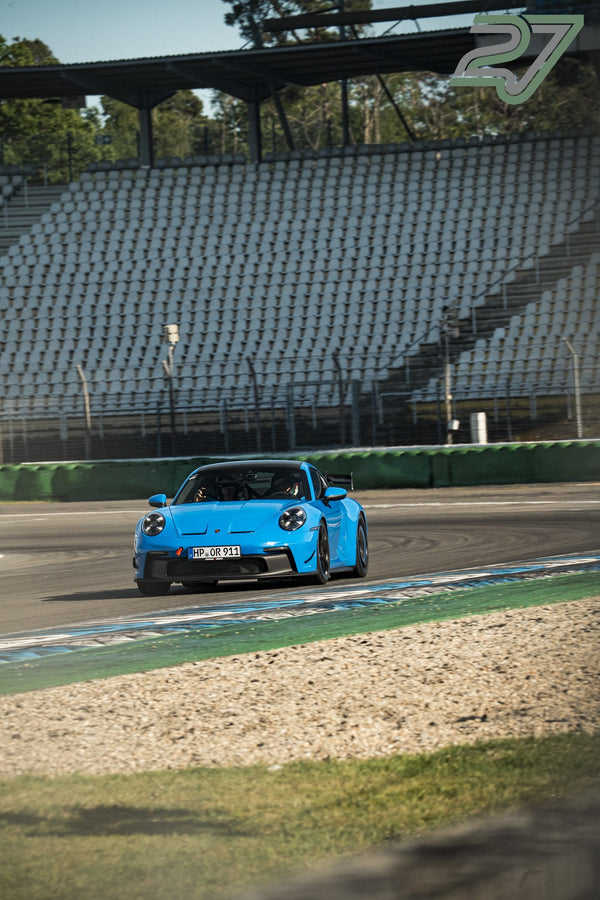 Hellblauer Porsche 911 GT3 mit Heckflügel fährt frontal auf die leere Tribüne zu
