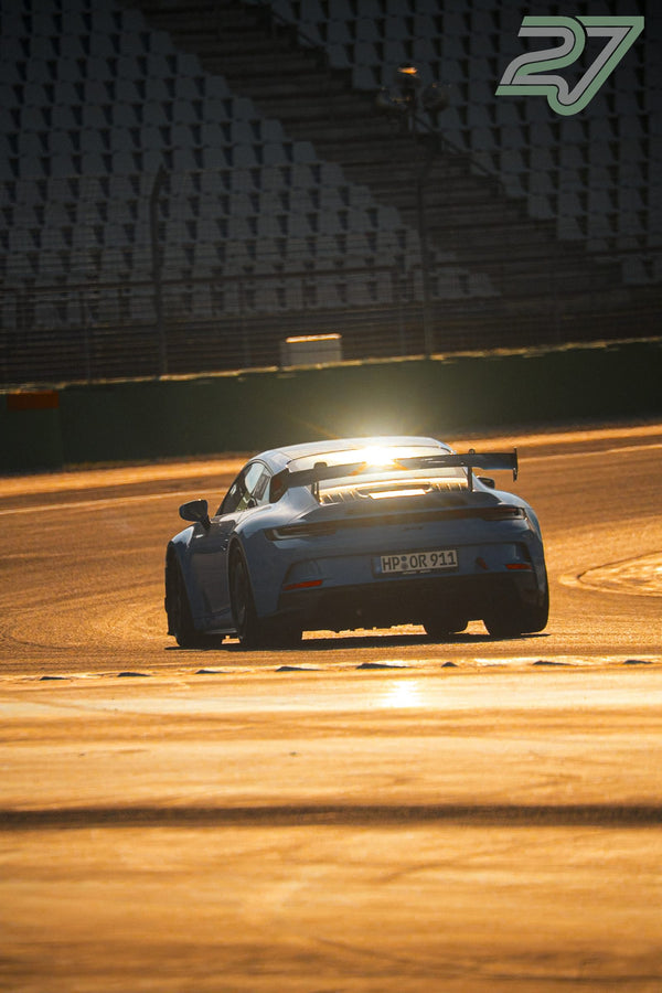 Blaugrauer Porsche 911 GT3 mit Heckflügel fährt von hinten in starkes Sonnenlicht