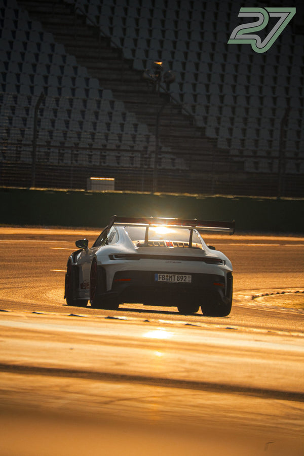 Weißer Porsche 911 GT3 RS fährt mit starkem Sonnenflare an der Tribüne vorbei
