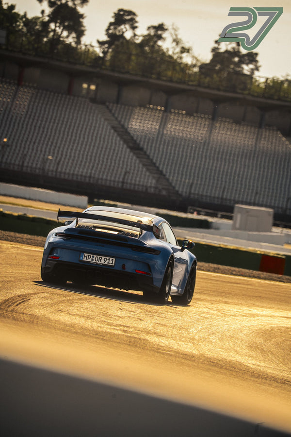 Blauer Porsche 911 GT3 mit großem Heckflügel hebt sich dunkel vom goldenen Asphalt ab