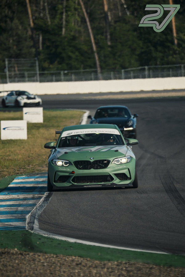 Salbeigrüner BMW M2 mit eingeschalteten Scheinwerfern fährt in warmem Abendlicht um die Kurve