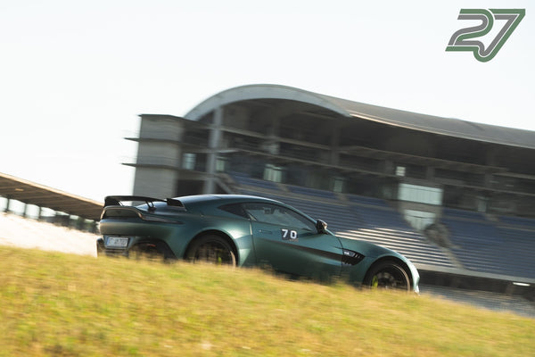Dunkelgrüner Aston Martin Vantage fährt vor der geschwungenen Hockenheimring-Tribüne