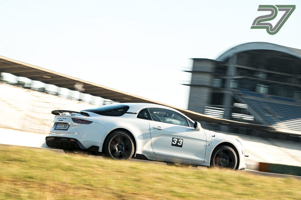 Weißer Alpine A110 mit Startnummer 33 fährt dynamisch vor der geschwungenen Tribüne vorbei
