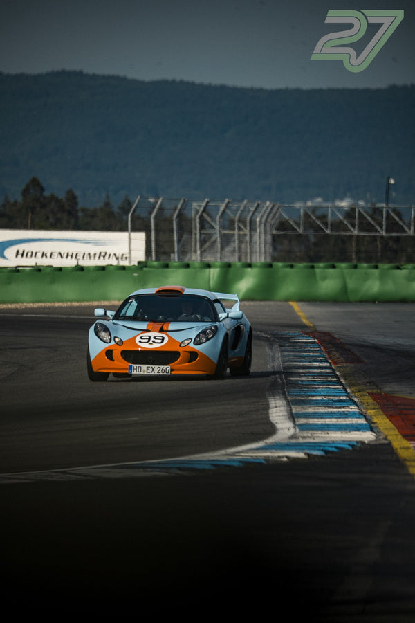 Hellblau-oranger Lotus Exige mit Startnummer 99 fährt vor dem Hockenheimring-Schriftzug