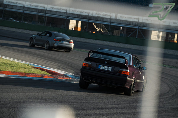 Dunkelroter BMW M3 fährt vor silbernem BMW 3er dynamisch aus der Kurve heraus