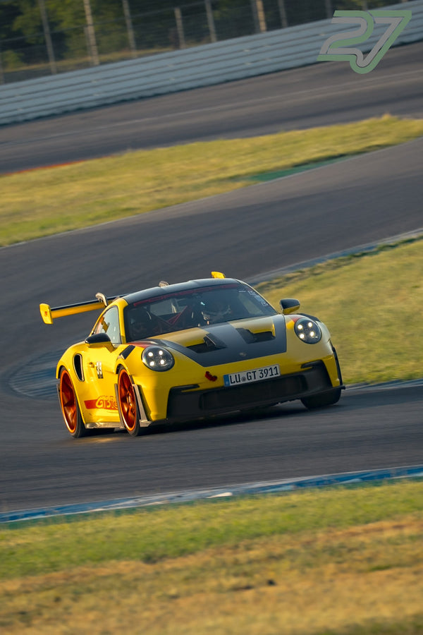 Gelber Porsche 911 GT3 RS mit orangefarbenen Felgen fährt dynamisch durch die Kurve