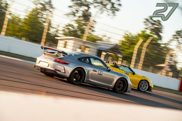 Silberner Porsche 911 GT3 fährt dicht vor einem gelben offenen Porsche durch eine Kurve