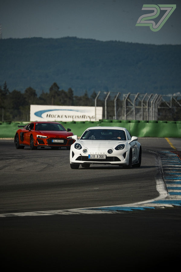 Weißer Alpine A110 führt rotorangenen Audi R8 in warmem Abendlicht durch die Kurve