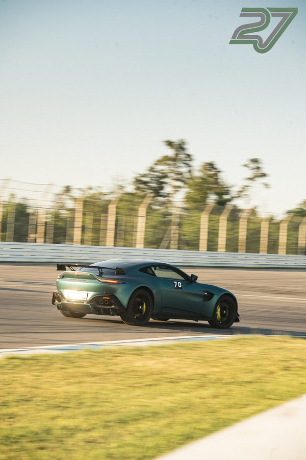 Dunkelgrüner Aston Martin Vantage neigt sich mit leuchtenden Scheinwerfern in die Kurve