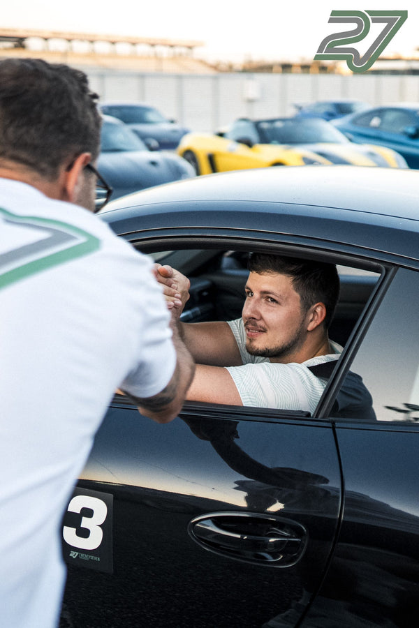 Mann begrüßt einen Fahrer durchs offene Fenster, im Hintergrund parken Rennwagen