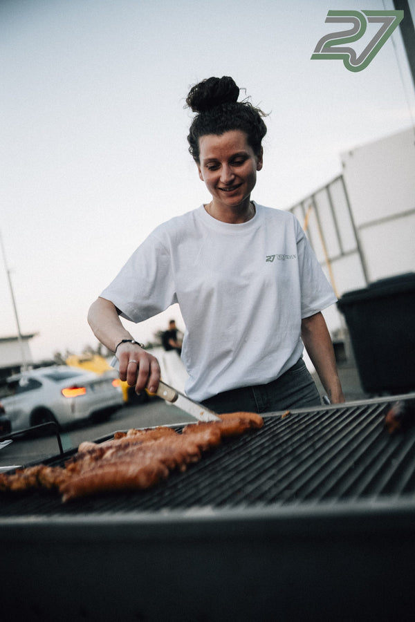 Lächelnde Frau im 27-Trackdays-Shirt wendet mit einem Messer Würstchen auf dem Grill