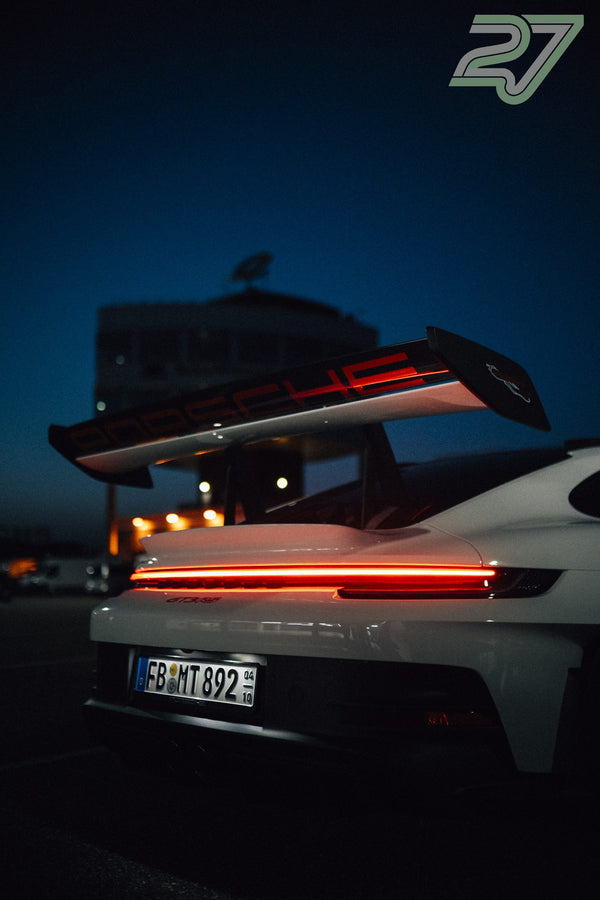 Weißer Porsche 911 GT3 mit leuchtendem Rücklichtband vor dunkelblauem Abendhimmel
