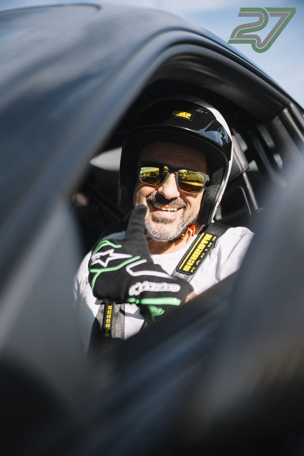 Fahrer mit Helm und Sonnenbrille lacht breit und hebt die behandschuhte Hand