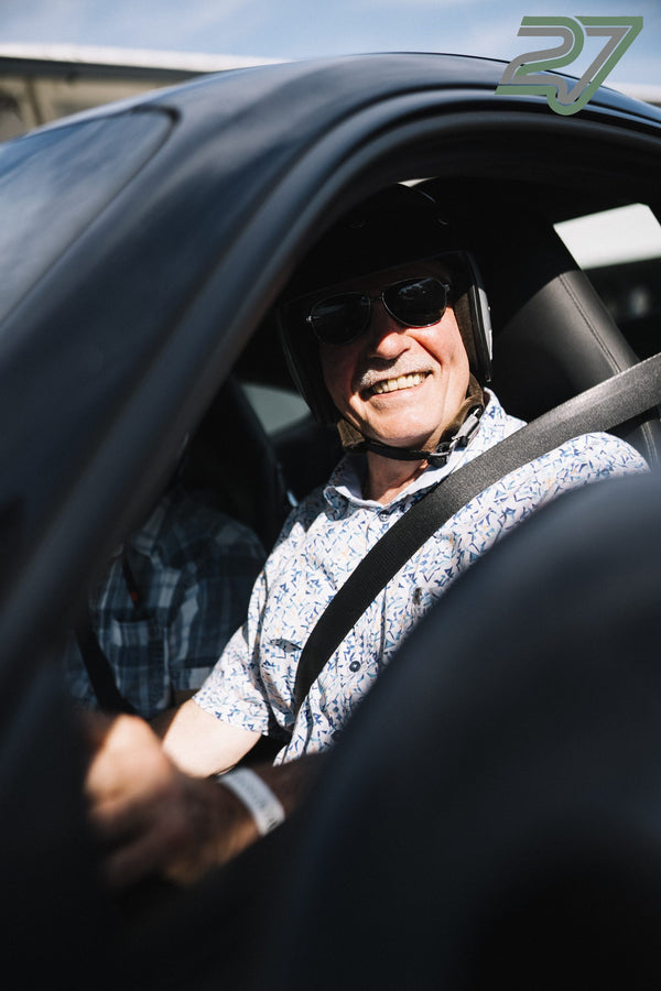Fahrer mit hochgeklapptem Helmvisier und Sonnenbrille lächelt sehr freundlich im Auto