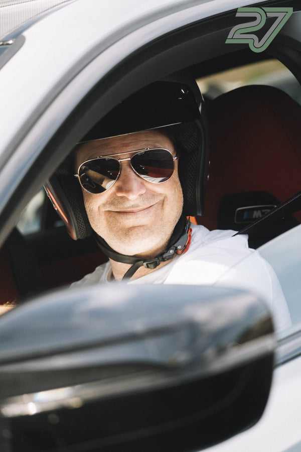 Lächelnder Fahrer mit Helm sitzt im BMW M3, der Seitenspiegel ist im Vordergrund unscharf