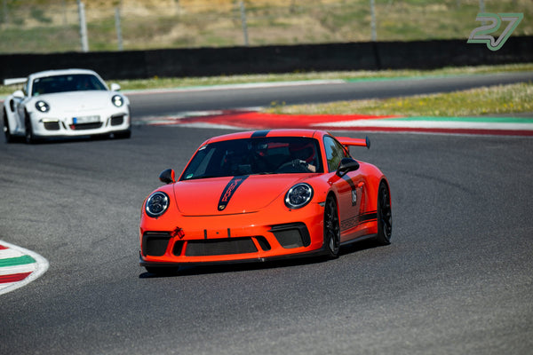 Ein orangeroter Porsche 911 GT3 führt vor einem weißen Porsche 911 GT3 RS durch die Kurve