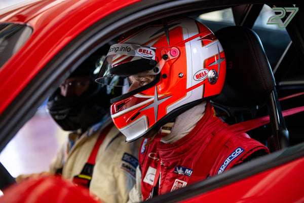 Blick durch das offene Fenster auf einen Fahrer mit rot-weißem Helm, daneben eine zweite Person
