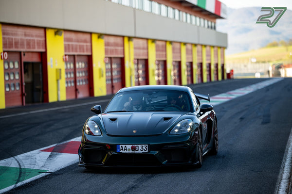 Dunkelgrüner Porsche 718 Cayman GT4 RS rollt frontal durch die Boxengasse, Daumen hoch am Steuer
