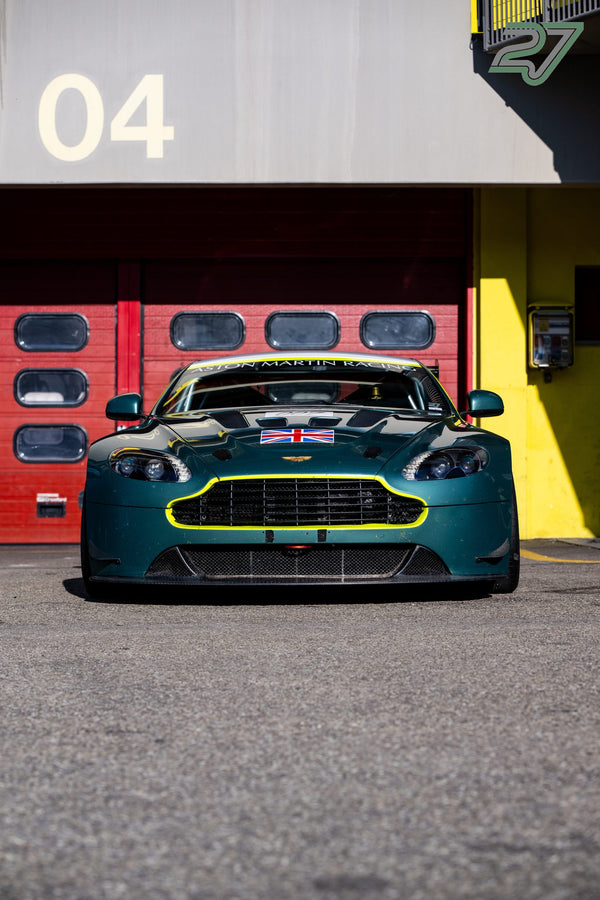 Dunkelgrüner Aston Martin mit Union Jack und gelben Akzenten vor dem roten Boxentor Nummer 04