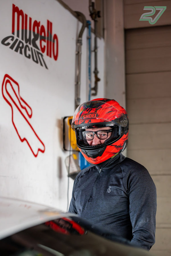 Mann mit rotem Helm und hochgeklapptem Visier vor der Wand mit Mugello-Logo und Streckengrafik