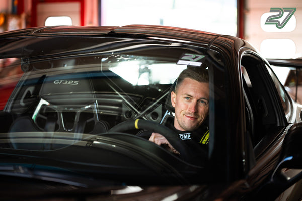 Fahrer im schwarzen Overall am Lenkrad eines dunklen Porsche 911 GT3 RS, Blick aus dem Seitenfenster