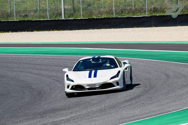 Weißer Ferrari mit blauem Doppelstreifen kommt frontal durch die Kurve, grün-weiße Randsteine