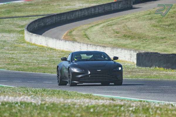 Dunkler Aston Martin Vantage frontal in der Kurve, dahinter schwingt die Strecke bergan