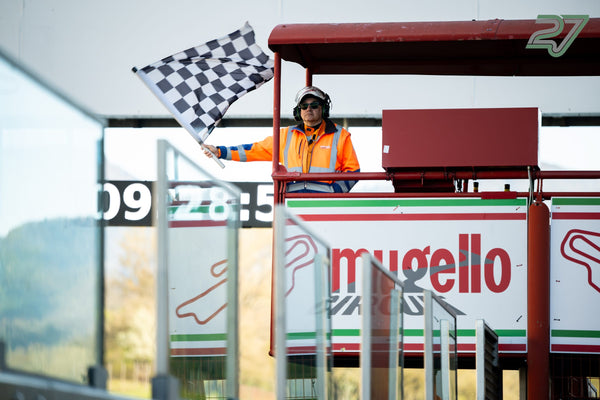 Streckenposten in Orange schwenkt die Zielflagge vom roten Podest über den Mugello-Banden