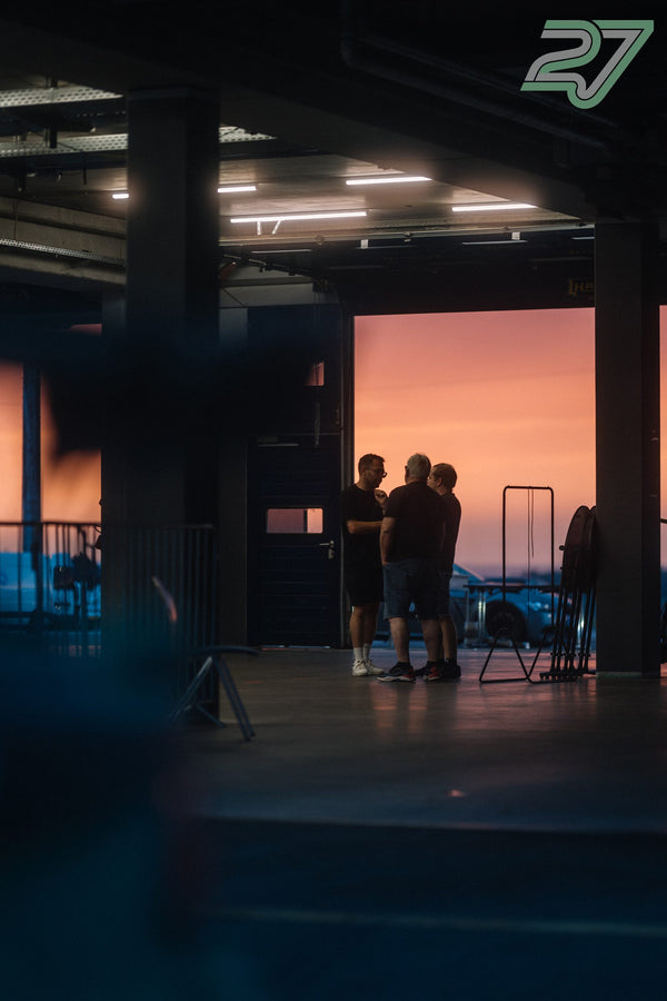 Drei Männer stehen im Gespräch vor dem geöffneten Boxentor, der Himmel leuchtet in Sonnenuntergangsfarben