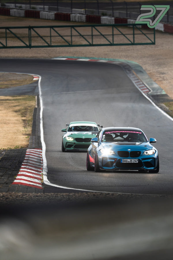 Blauer BMW M2 mit Scheinwerferlicht führt vor mint-grünem BMW M2 durch eine Kurve am Nürburgring