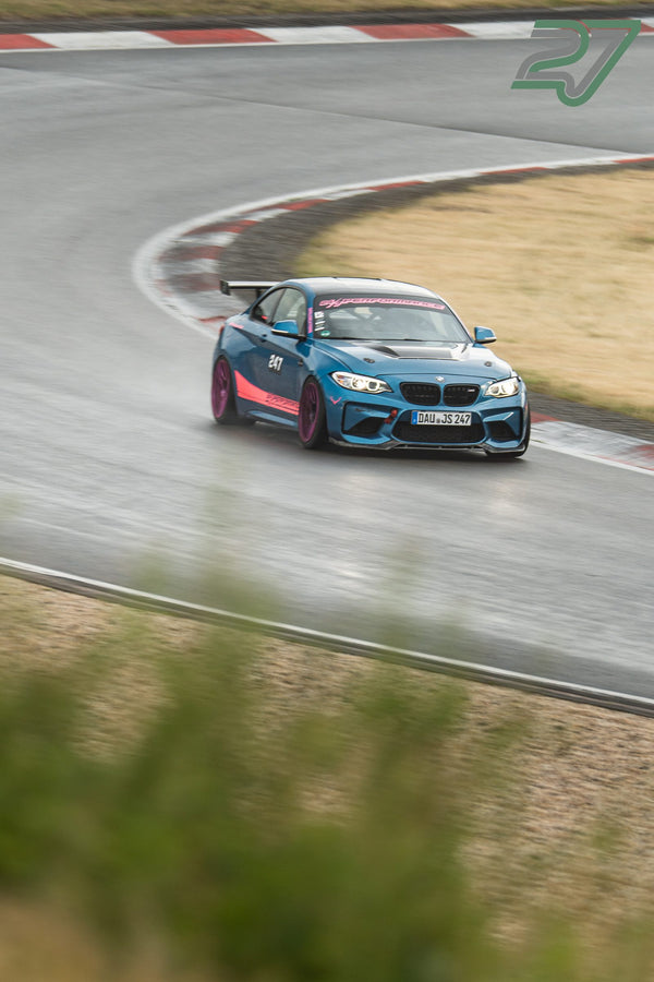 Dunkelblauer BMW M2 mit pinkfarbenen Streifen driftet auf dem nassen Nürburgring durch die Kurve