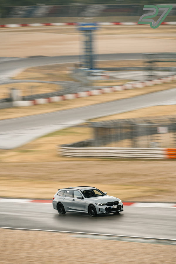 Silberner BMW Touring zieht mit Schwung durch eine weite Kurve auf regennasser Fahrbahn