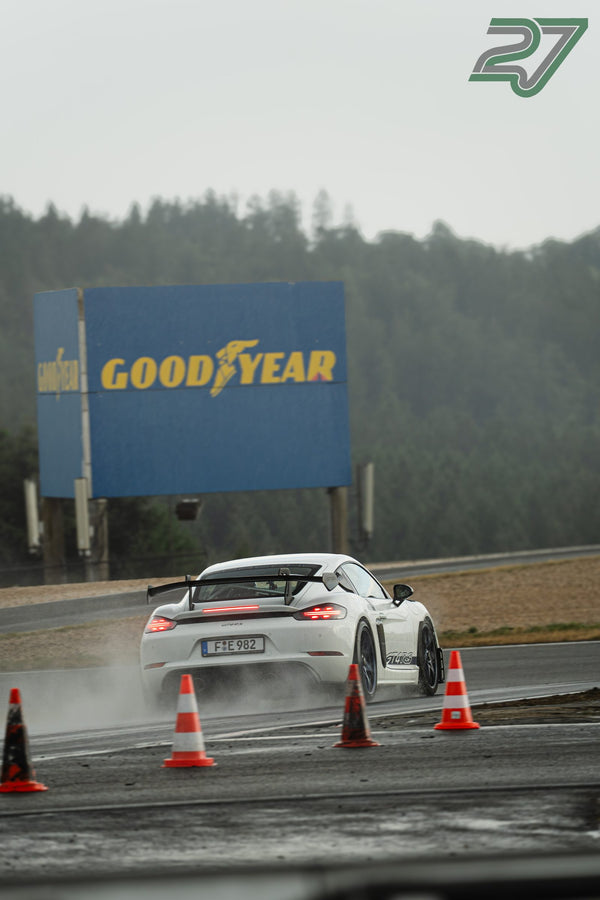 Weißer Porsche Cayman GT4 RS driftet mit Gischt zwischen Pylonen auf dem nassen Nürburgring