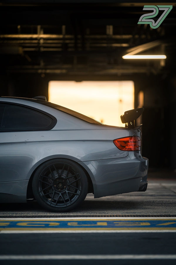 Silbergrauer BMW M3 mit Heckflügel steht im warmen Gegenlicht einer geöffneten Boxentür