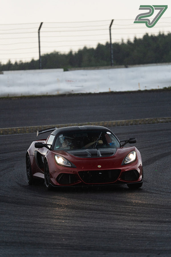 Dunkelroter Lotus Exige zieht mit Scheinwerferlicht durch Regen und spiegelnde Nässe