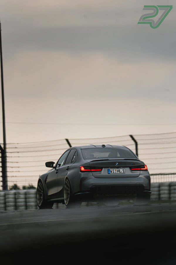 Grauer BMW M3 rollt im warmen Abendlicht mit leuchtenden Rückleuchten von hinten ins Bild