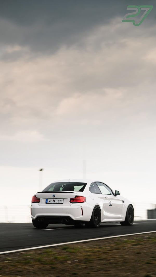 Weißer BMW M2 zieht in scharfer Panning-Aufnahme unter bewölktem Himmel vorbei
