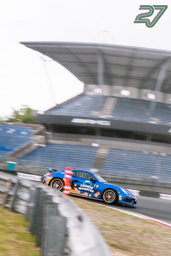 Blauer Porsche mit Cookie-Monster-Lackierung zieht in scharfer Panning-Aufnahme vor der Tribüne