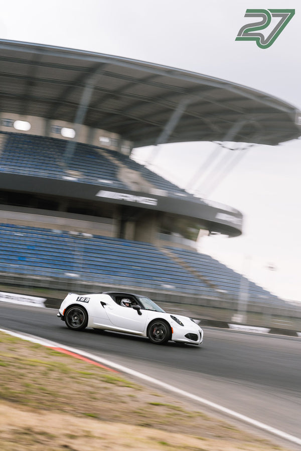 Weißer Alfa Romeo 4C zieht in dynamischer Panning-Aufnahme vor der blauen Tribüne vorbei