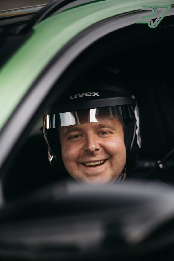 Fahrer im grünen Auto lacht breit mit offenem Helmvisier direkt in die Kamera