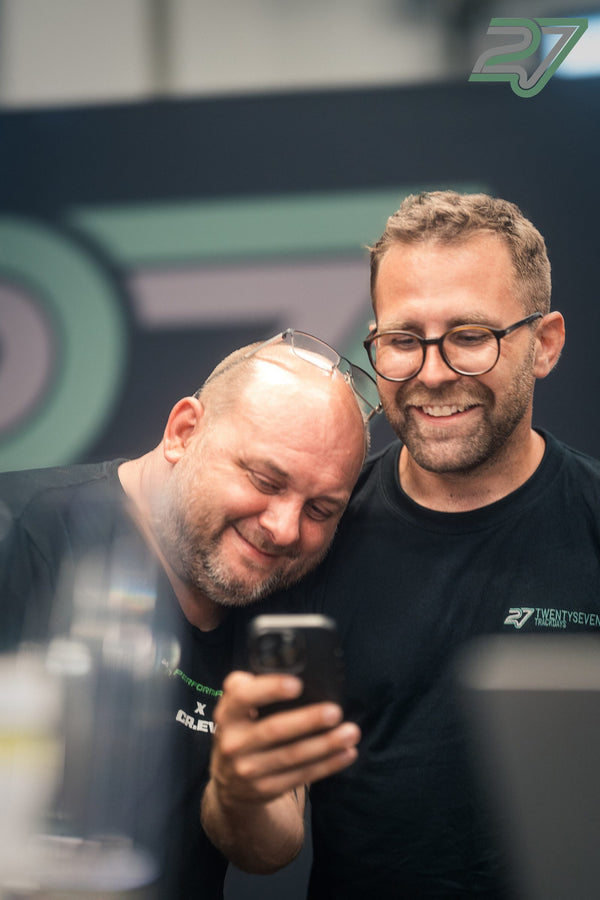 Zwei Männer lachen gemeinsam über ein Foto auf dem Handy in der Trackday-Halle