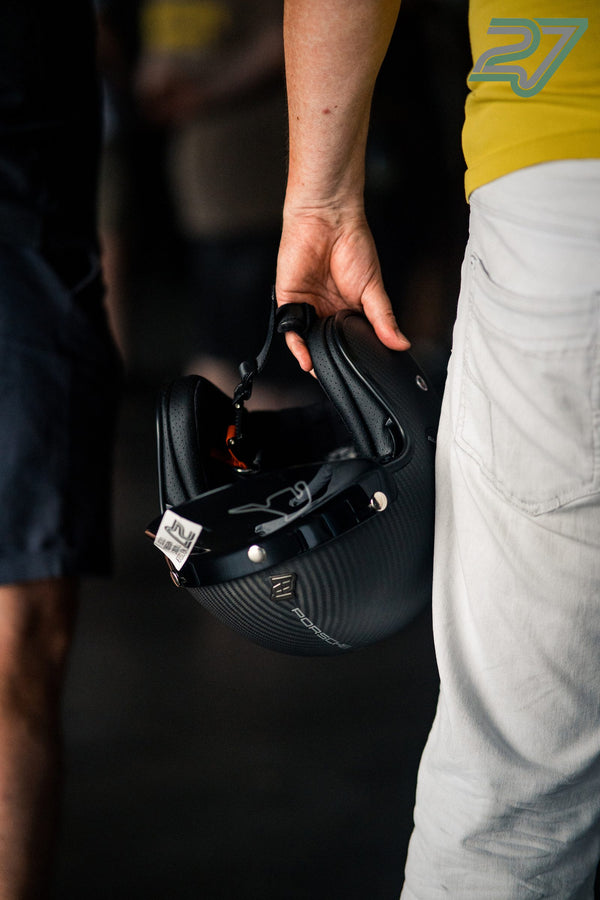 Eine Hand hält einen schwarzen Porsche-Helm in Nahaufnahme vor unscharfem Hintergrund