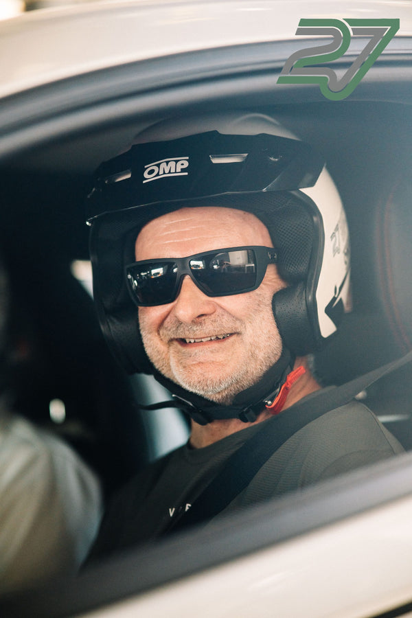 Älterer Fahrer mit schwarzem Helm und dunkler Sonnenbrille lächelt breit im Fahrzeug