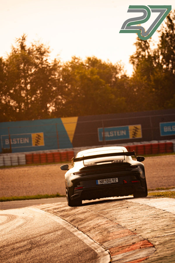 Schwarzer Porsche 911 fährt als Heck-Silhouette im Sonnenuntergang über die Strecke