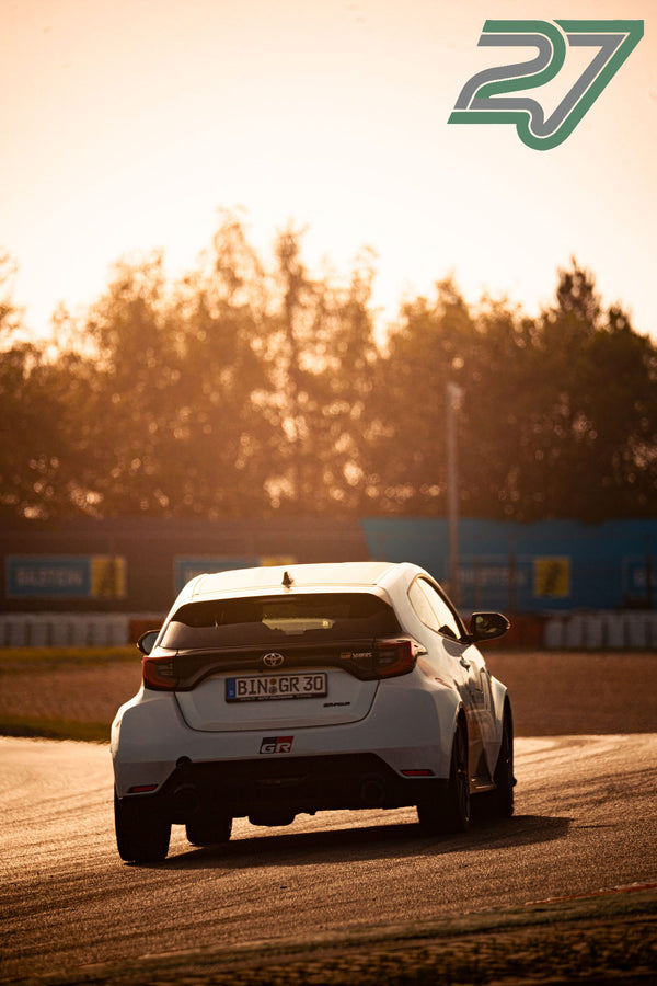 Weißer Toyota GR Yaris fährt im Gegenlicht bei Sonnenuntergang über die Strecke