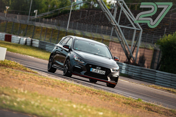 Dunkelgrauer Hyundai i30 N lenkt in eine Kurve vor der verwitterten Tribüne am Nürburgring