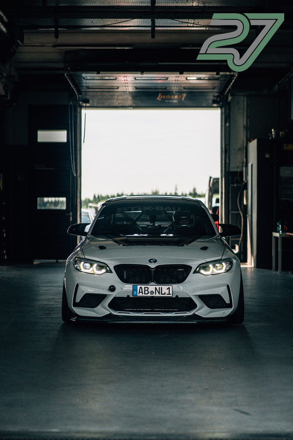 Weißer BMW M2 steht mit leuchtenden Scheinwerfern symmetrisch in der geöffneten Box
