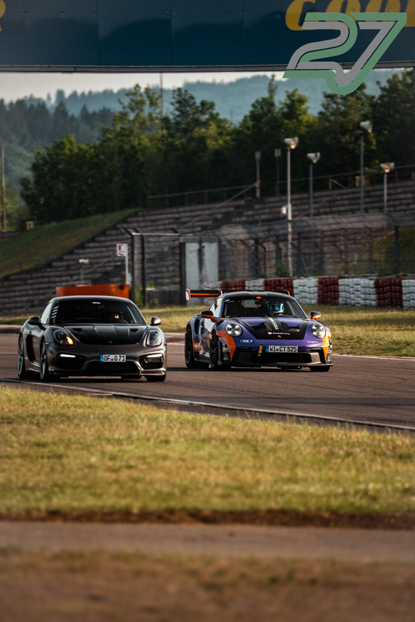 Grauer Porsche Cayman und lila-oranger Porsche 911 GT3 Cup fahren dicht hintereinander durch eine Kurve