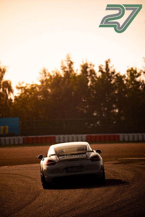 Weißer Porsche Cayman fährt mit dramatischem Gegenlicht die Boxengasse entlang, Heckansicht