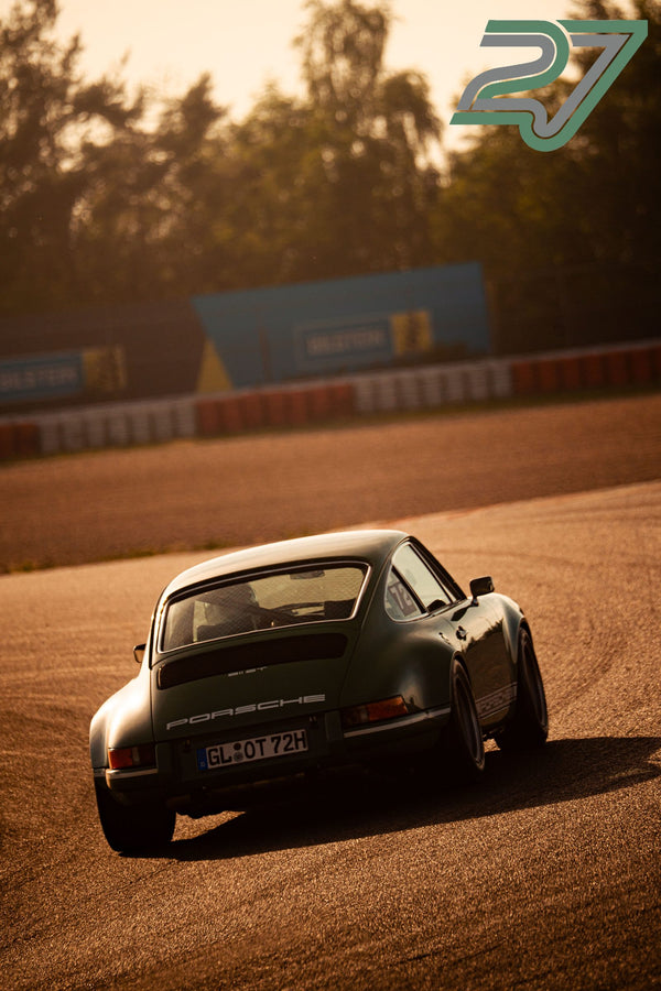 Dunkelgrüner klassischer Porsche 911 fährt im goldenen Gegenlicht durch eine Kurve am Nürburgring